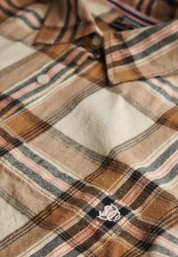 Brązowa koszula w kratę z guzikami, wykonana z miękkiego materiału, z jasną kremową, różową i czarną linią oraz małym haftowanym logo na piersi.