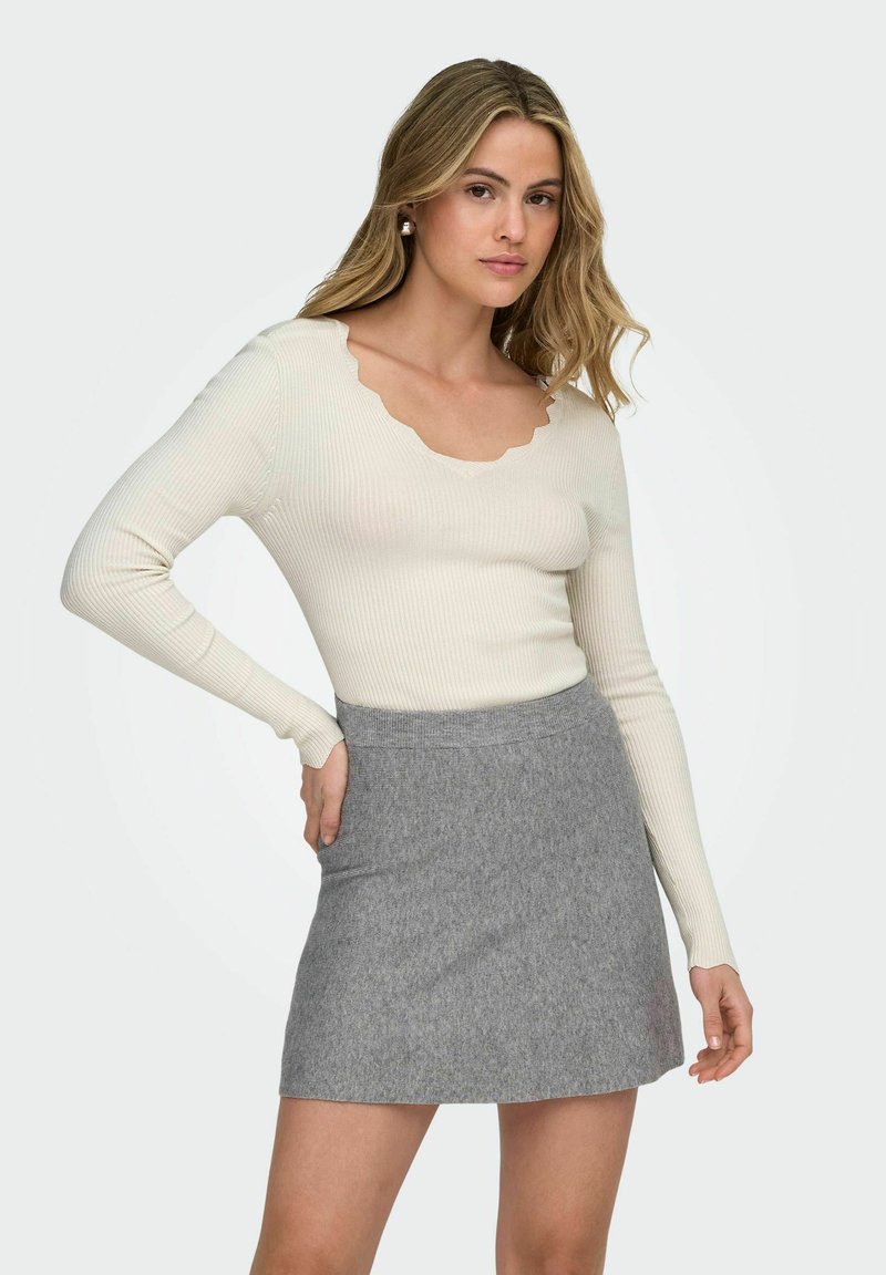 Jasno beżowa, prążkowana bluzka z długim rękawem i falbaniastym dekoltem, zestawiona z szara, obcisłą spódnicą. Gładka tekstura, prosty design i dopasowany krój.