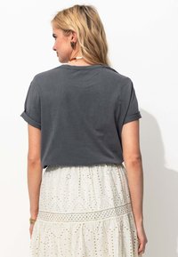 T-shirt en coton gris avec des manches retroussées, présenté de dos, associé à une jupe en eyelet blanche avec des découpes décorées et des accents en dentelle.
