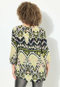 Tunic multicolore con un motivo verde, rosa e nero, dotata di maniche a tre quarti e scollatura arrotondata, realizzata in tessuto leggero.