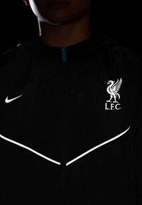 Czarna kurtka przeciwdeszczowa z odblaskowymi akcentami, logo Nike i herb Liverpool FC, z zamkiem błyskawicznym z przodu oraz z kapturem.