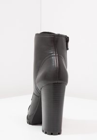 Botín de cuero negro hasta el tobillo con un tacón alto y texturizado, cremallera lateral y acabado suave. Presenta costuras curvas y una suela robusta.