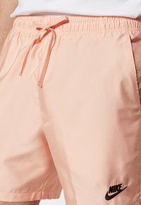 Shorts Nike pink clair avec ceinture élastique et cordon de serrage, portés par une personne les mains dans les poches.