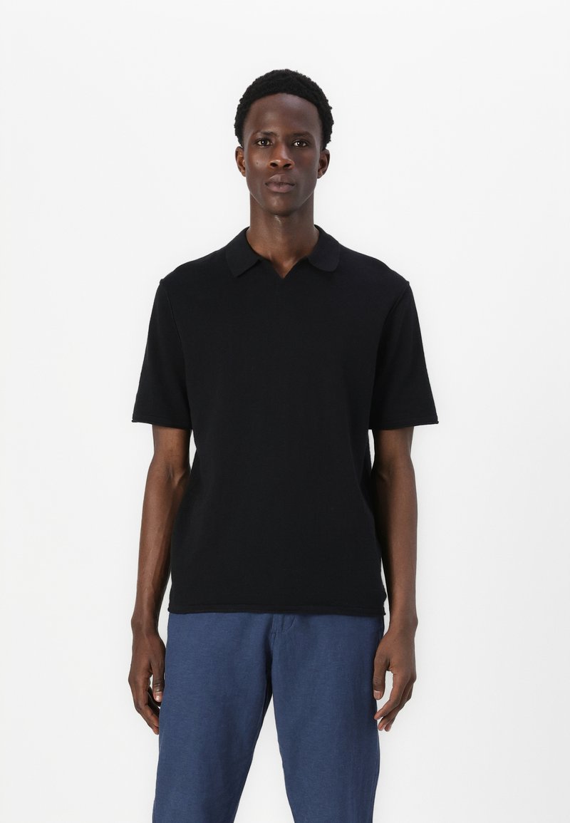 Svart polo skjorte med en myk tekstur, korte ermer og en klassisk krage, sammen med marineblå bukser. Enkel, minimalistisk design.