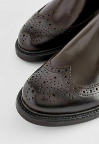 Brune lædersko med perforerede detaljer, rund tå og en blank finish. Sort sål med syet kant. Klassiske brogue-designelementer.
