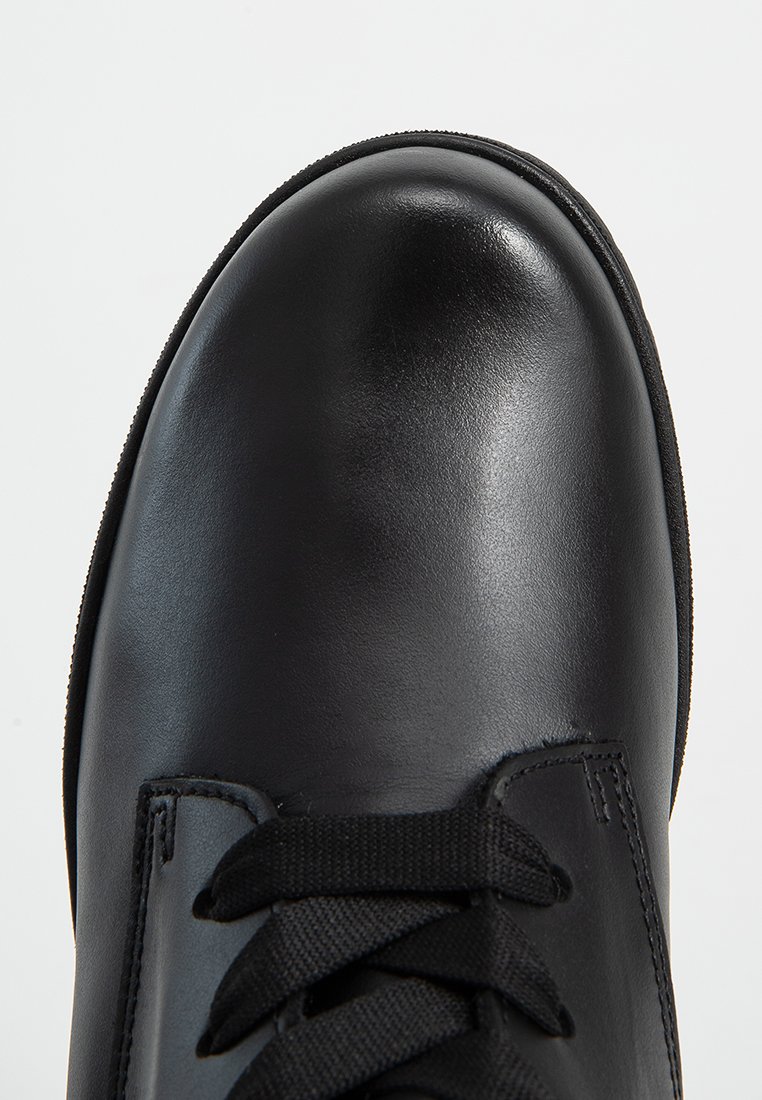 Schwarzer Lederschuh mit runder Zehenform und schwarzen Schnürsenkeln, von vorne oben auf einem weißen Hintergrund gezeigt.