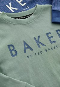 Világoszöld pulóver, sötétkék "BAKER" felirattal, kerek nyakkal, puha tapintású, mögötte egy réteges sötétkék mintás anyaggal.