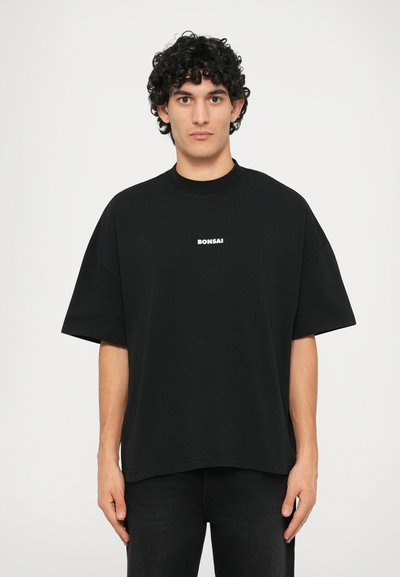 Zwarte oversized t-shirt met een hoge ronde hals. Heeft korte mouwen en een witte bedrukte "BONSAI" logo op de borst. Casual katoenen stof.