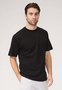 Sort bomuld t-shirt med korte ærmer, rund hals og en afslappet pasform. Bemærkelsesværdig glat tekstur og minimalistisk design. Parret med grå sweatpants.