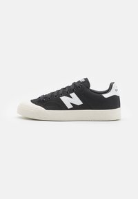 Valkoinen ja musta New Balance -lenkkari, jossa on kanvaalikotelo, valkoinen kumipohja ja valkoinen "N"-logo sivulla, nähtynä ulkosivulta.