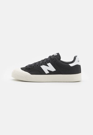 Czarno-białe sneakersy New Balance z płóciennym wykończeniem, białą gumową podeszwą i białym logo „N” po boku, widoczne od zewnętrznej strony.