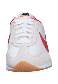 Zapatilla blanca con acentos rojos, que presenta una puntera de ante texturizado, parte superior sintética suave y suela de goma con un dibujo de tracción. Logotipo de Nike en la lengüeta.