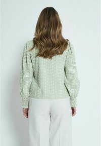 Ljusgrön blus med mönster och texturerade ränder, puffärmar och elastiska manschetter, i kombination med beiga vida byxor.