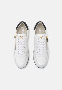 Fehér bőr sportcipők fekete díszítéssel, arany cipzár részlettel, fehér fűzőkkel és strukturált felülettel. Lapos gumi talpak.