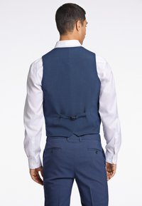 Marineblaues Anzugweste aus strukturiertem Stoff, mit einem höheren Rücken und einem Taillenverstellriemen, darunter ein weißes Langarmhemd.
