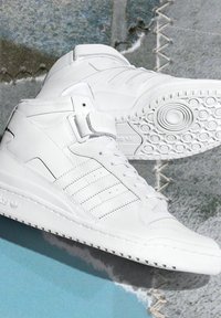 White high-top sneakers with a smooth leather upper, lace-up design, hook-and-loop strap, and textured rubber sole featuring circular patterns.