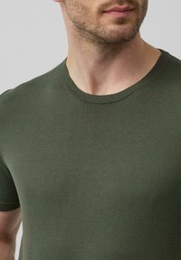 Zielony t-shirt z okrągłym dekoltem wykonany z teksturowanej tkaniny. Projekt posiada krótkie rękawy i dopasowany krój, odpowiedni do codziennego noszenia.