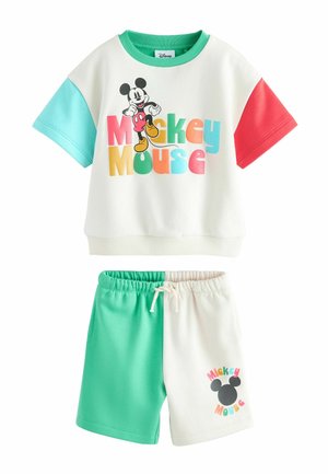 Mladý chlapec, ktorý má na sebe farebné tričko Mickey Mouse s červenými, žltými, zelenými a tyrkysovými rukávmi, pozerá mierne nahor s neutrálnym pozadím.