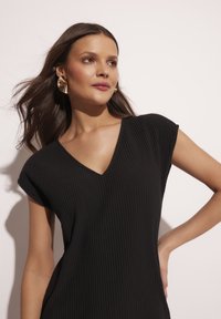 Czarna sukienka o prążkowanej fakturze, z dekoltem w serek i krótkimi rękawami, charakteryzująca się miękką teksturą i dopasowanym krojem. Złote, wyraziste kolczyki uzupełniają całość.