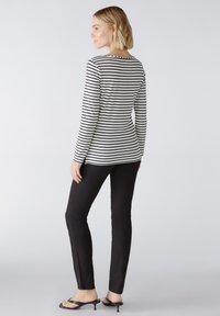 Zwart-wit gestreepte lange mouwen top met een ronde halslijn, gecombineerd met strakke zwarte broek en open teen zwarte hakken.
