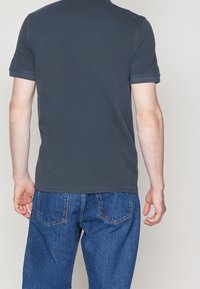 Czarna bawełniana koszulka z okrągłym dekoltem, krótkimi rękawami i luźnym krojem, w zestawieniu z niebieskimi dżinsami z tylnymi kieszeniami.