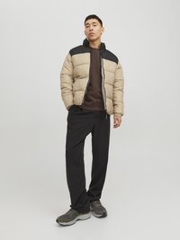 Giacca imbottita con un design a blocchi di colore beige e nero. Presenta un colletto alto, chiusura con zip ed è abbinata a pantaloni scuri e sneakers grigie.