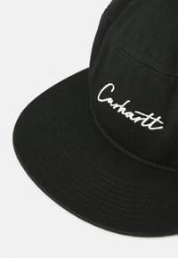 Black baseball cap made of textured fabric features a curved brim and white embroidered "Carhartt" logo on the front panel.