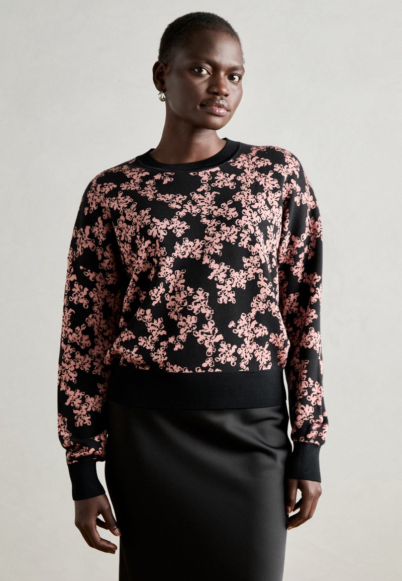 Črni pleteni pulover s cvetličnim rožnatim vzorcem, rebrastim okroglim izrezom in dolgimi rokavi, v kompletu z gladko črno krilom.