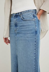 Ljusblå denimkjol med rak skärning, hög midja, sidofickor och subtila blekningar. Bärs med en vit ribbad topp och en randig jacka.