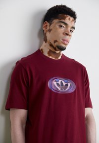 Bordeauxkleurig T-shirt met korte mouwen en een rond logootje met overlappende blauwe en witte elementen op de borst. Gemaakt van zachte katoen.