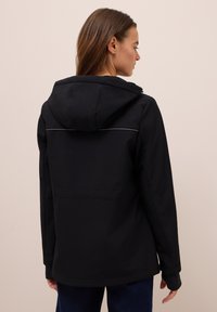 Zwarte hoodie met een gladde textuur, voorzien van een rugpasdetail en een subtiele reflecterende bies langs de naad.