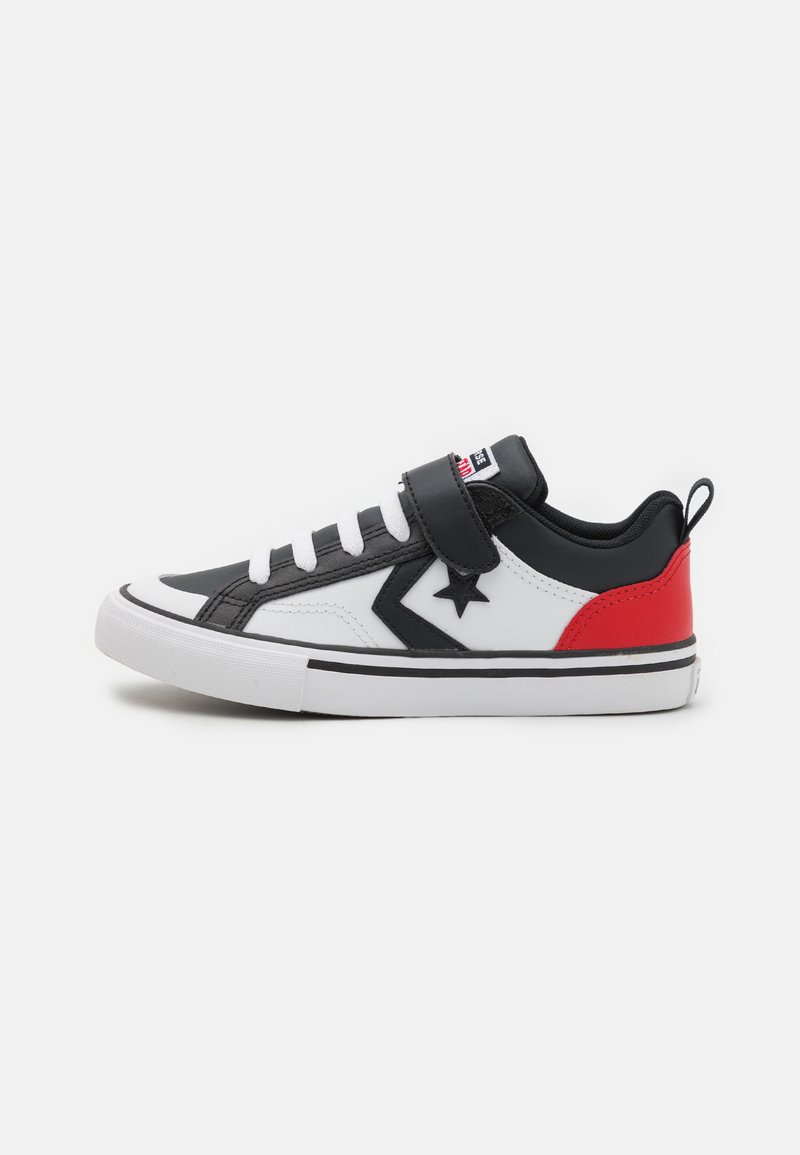 Sneaker bianco e nero con accenti rossi, dotato di una tracolla in velcro, suola in gomma e un emblema a stella sul lato. Materiale superiore testurizzato.