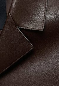 Brązowy skórzany materiał o teksturowym wykończeniu. Posiada złożoną klapkę i widoczne szwy wzdłuż krawędzi, podkreślające szczegóły rzemiosła.