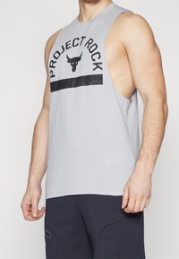 Camiseta sin mangas de color gris claro hecha de algodón, que presenta un gráfico negro de "PROJECT ROCK" y un logo de toro en la parte delantera.