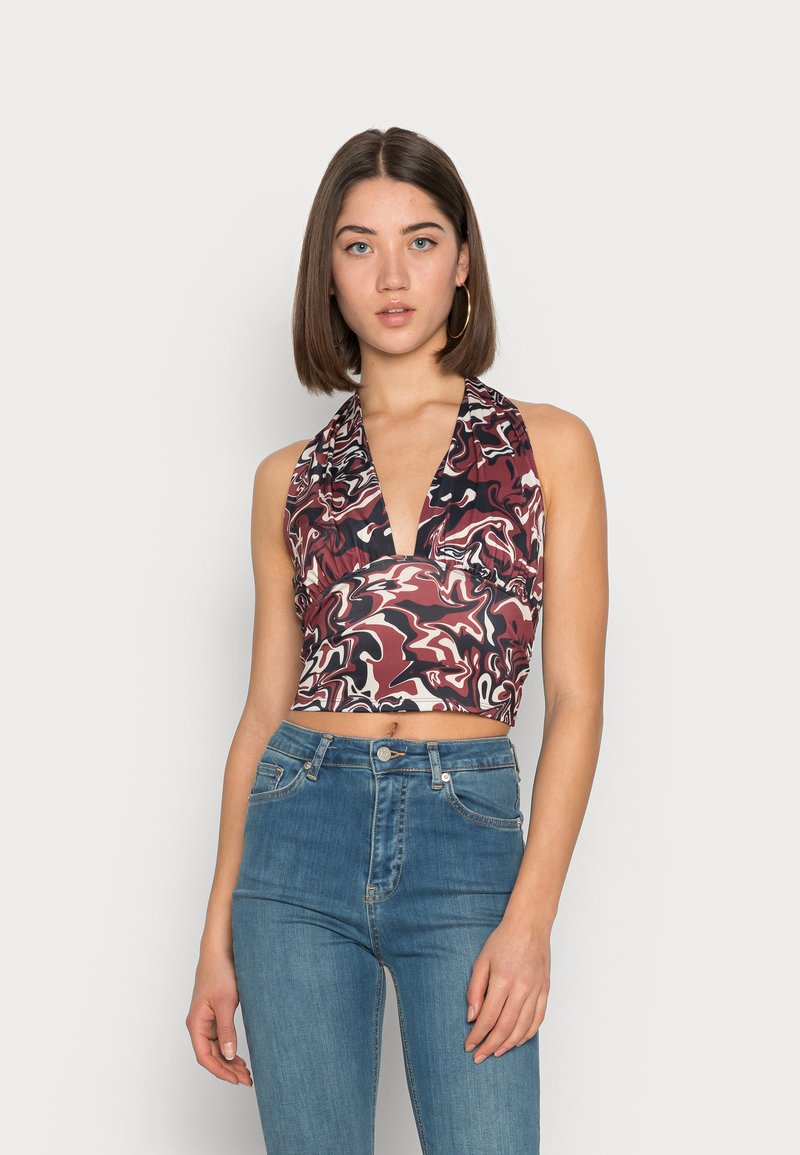 Top halter cropped em padrão abstracto multicolorido com decote em V profundo. Combinado com jeans de ganga azul de cintura alta. Textura suave, design ajustado.