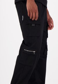 Schwarze Cargo-Shorts mit mehreren Taschen, einer Reißverschlusstasche am Bein und einem lässigen Schnitt. Hergestellt aus robustem Material mit glatter Textur.