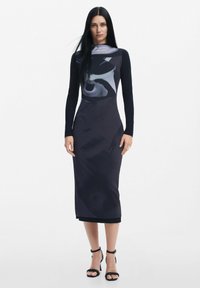 Rochie neagră cu mânecă lungă, având un model abstract gri, siluetă mulată și un despicat pe lateral, completată de tocuri negre cu bretele.