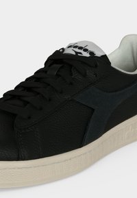 Baskets en cuir noir avec lacets noirs, bande latérale foncée, étiquette blanche sur la languette et semelle texturée blanc cassé.