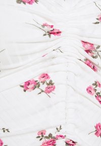 Blommönstrad topp i vitt, med rosa rosor och gröna blad. Samlad design med subtil textur och ribbad detalj.