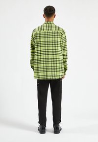 Groene en zwarte geruite oversized blouse met een knoopsluiting en rechte zoom, gemaakt van zachte stof. Gemaakt in combinatie met zwarte broeken en schoenen.