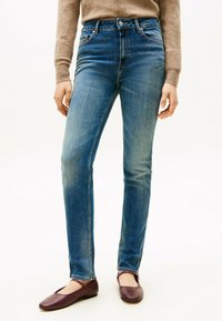 Jeans de mezclilla azul con un diseño de pierna recta, talle medio y un ligero desvanecimiento. Combinados con zapatos planos burdeos.