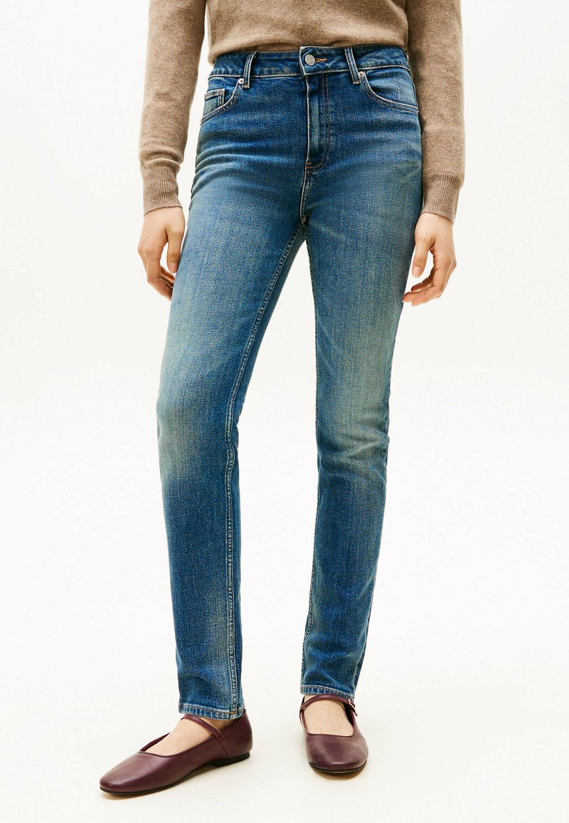 Jeans de mezclilla azul con un diseño de pierna recta, talle medio y un ligero desvanecimiento. Combinados con zapatos planos burdeos.