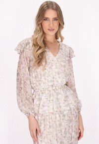 Licht doorschijnende jurk met bloemenpatroon, een V-hals, rimpel mouwen en een elastische taille, in zachte pasteltinten van roze en beige.