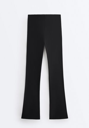 Pantaloni negri cu talie înaltă, ușor evazați la bază, așezați pe o suprafață albă.