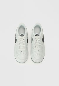 Valged Nike Air spordijalatsid mustade swoosh aktsentidega, aukudega varbalähedus, sile naha ülemine osa ja lapikud paelad. Spordistiil, millel on pehmendusega kaelus.