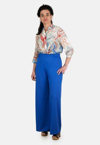 Pantalones amplios de color azul con cinturilla elástica, combinados con una blusa larga de manga larga de patrón jaspeado en tonos rojos, azules y blancos.