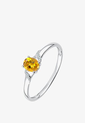 Hopeasormus, jonka keskellä on soikea keltainen jalokivi, ja sen molemmin puolin pienet kirkkaat kimaltelevat koristeet.