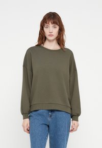 Olive green oversized sweatshirt with a round neckline and dropped shoulders. Ribbed cuffs and hem, made from a soft fabric. Paired with blue jeans.