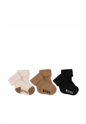 Trois paires de chaussettes bébé pliées en beige, marron et noir, chacune avec "BOSS" écrit sur la zone des orteils.