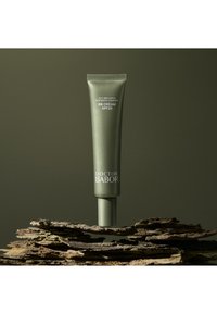 Tubo verde de crema BB con SPF 20, con el logo embosado "Doctor Babor", colocado sobre una corteza texturizada con un fondo oscuro.
